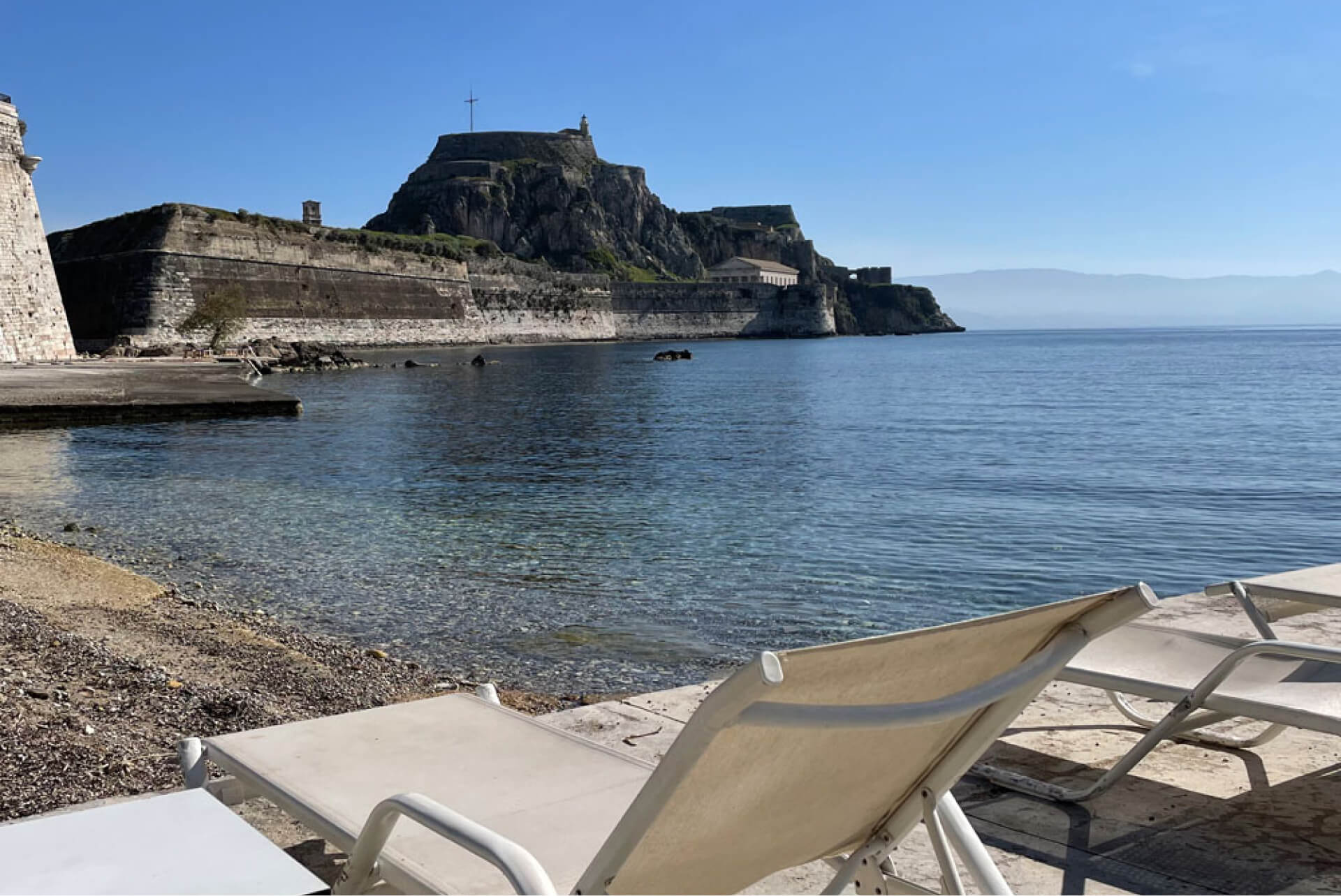 Scenic beach view from Naok Azure with sunbeds overlooking the old fortress of Corfu